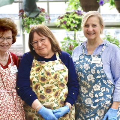 three women in aprons smile with plants behind them