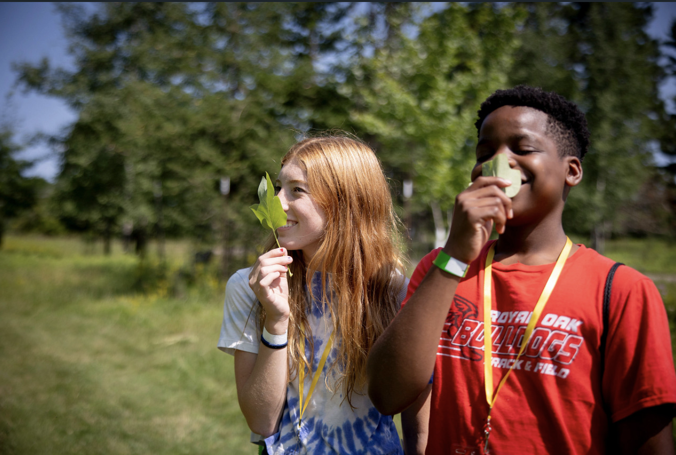 Two young teens smil as they hold leaves up to their faces