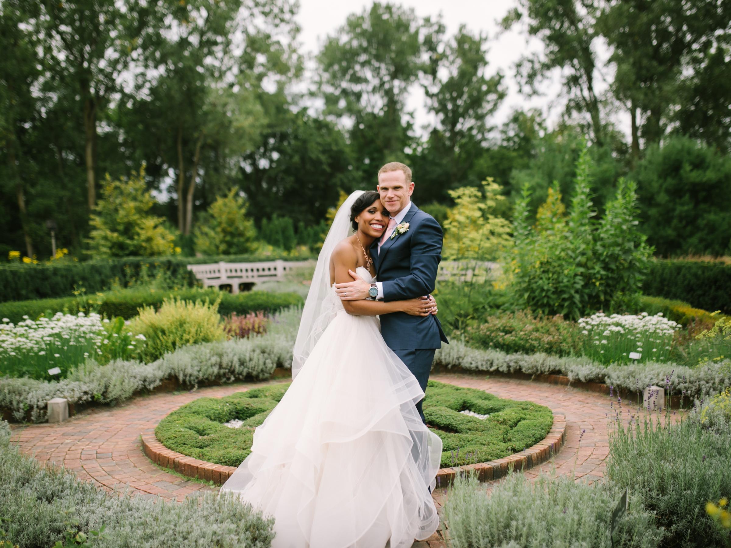 two people in wedding clothes embrace in herb knot garden