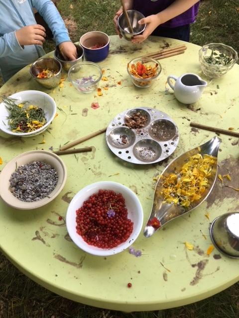 A child sized table with many bowls with a variety of natural materials.  Small hands hold bowls