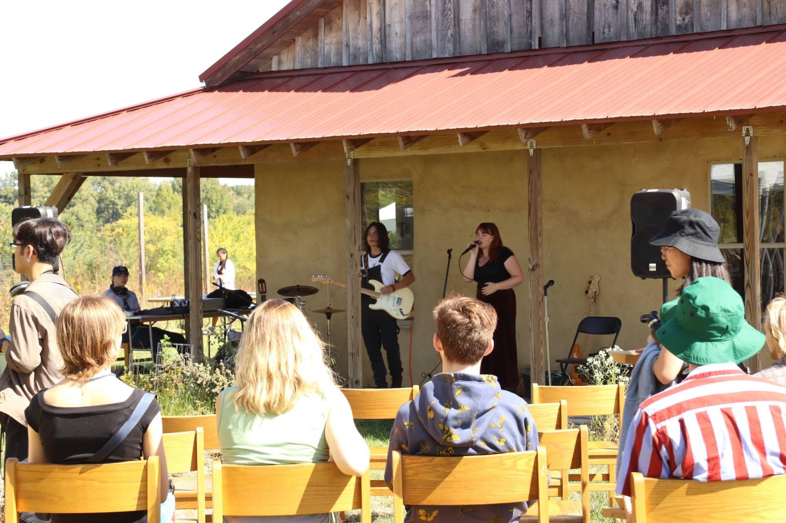 people watching.a band play in front of straw bale house at campus farm