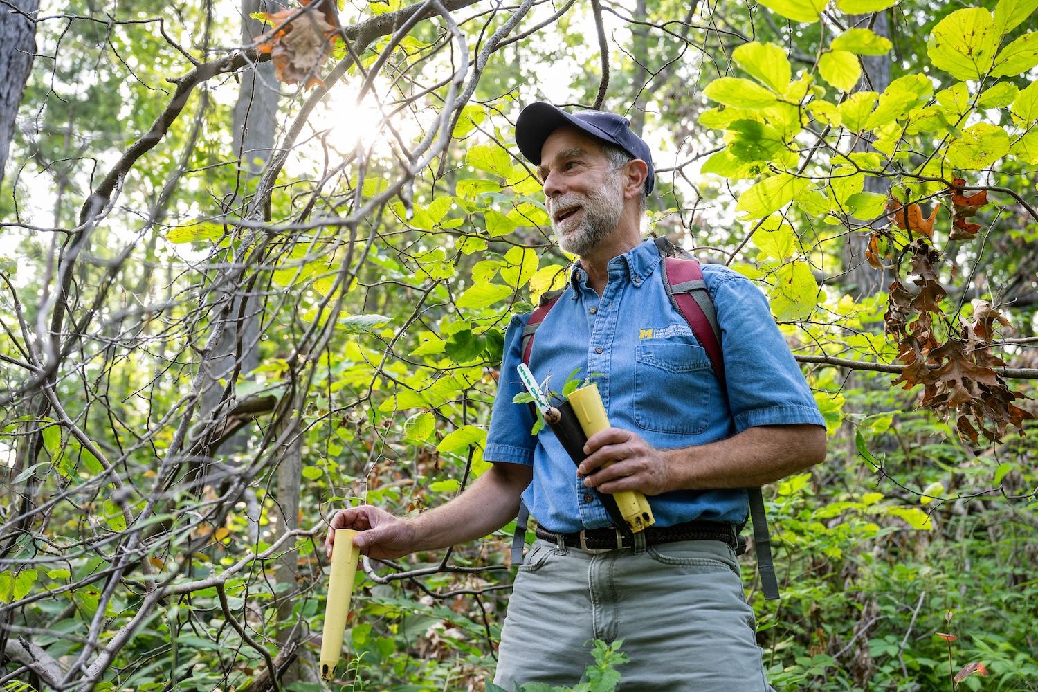Mike Kost in woods holding small oak seedlings