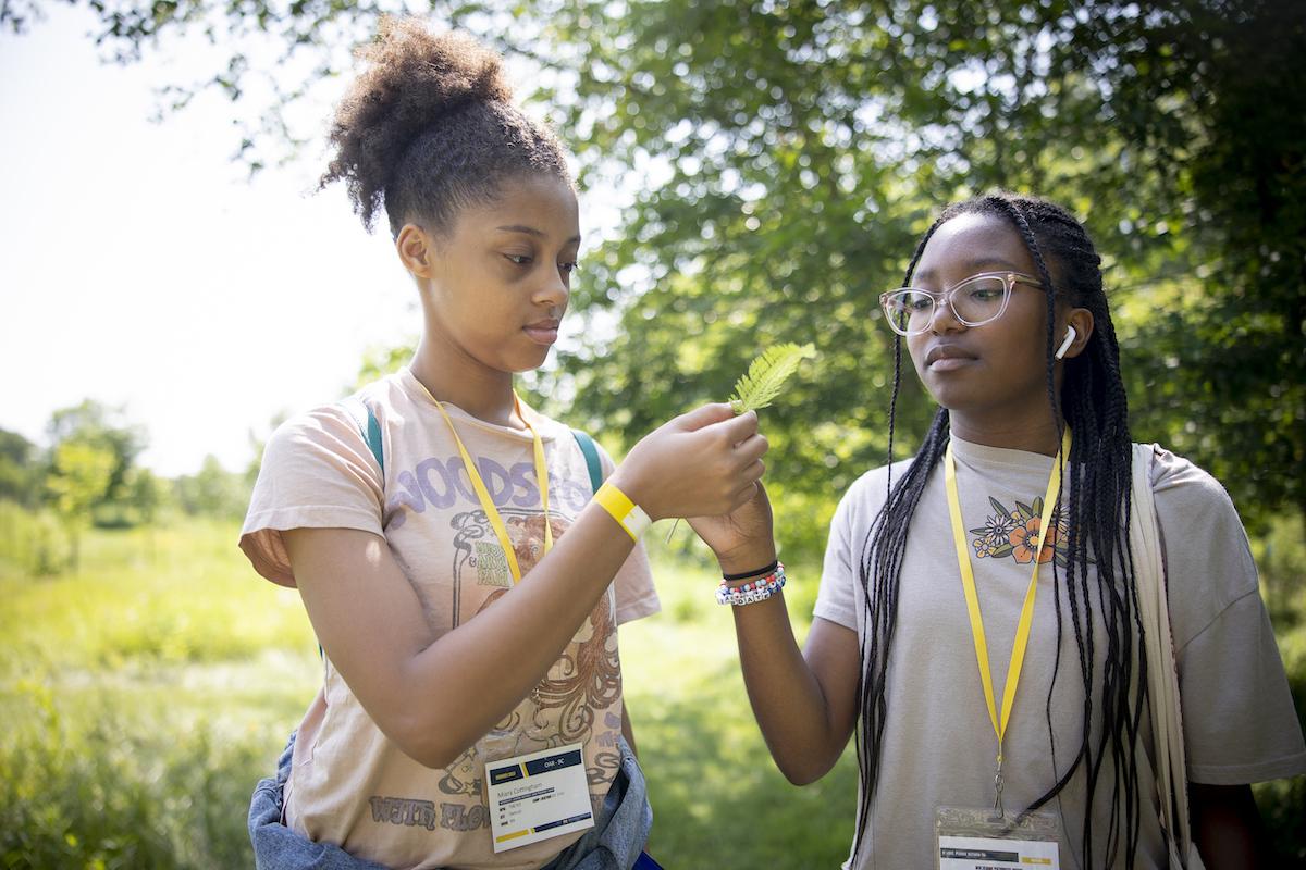 two teens outside hold up and look at a leaf