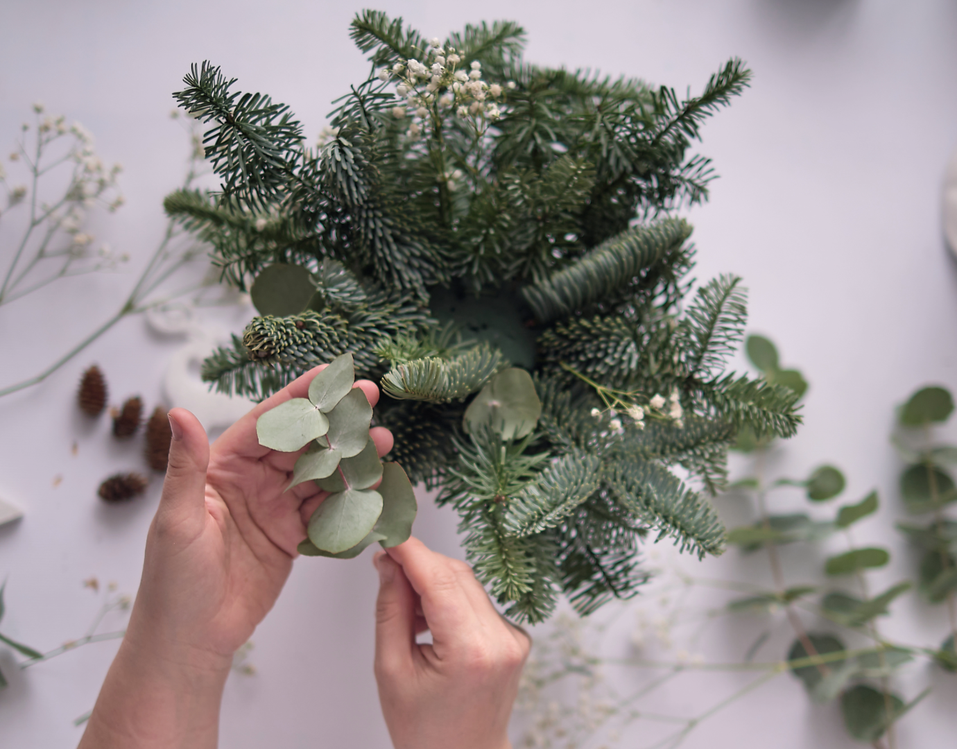 pair of hands putting together an arrangement of holiday greens 