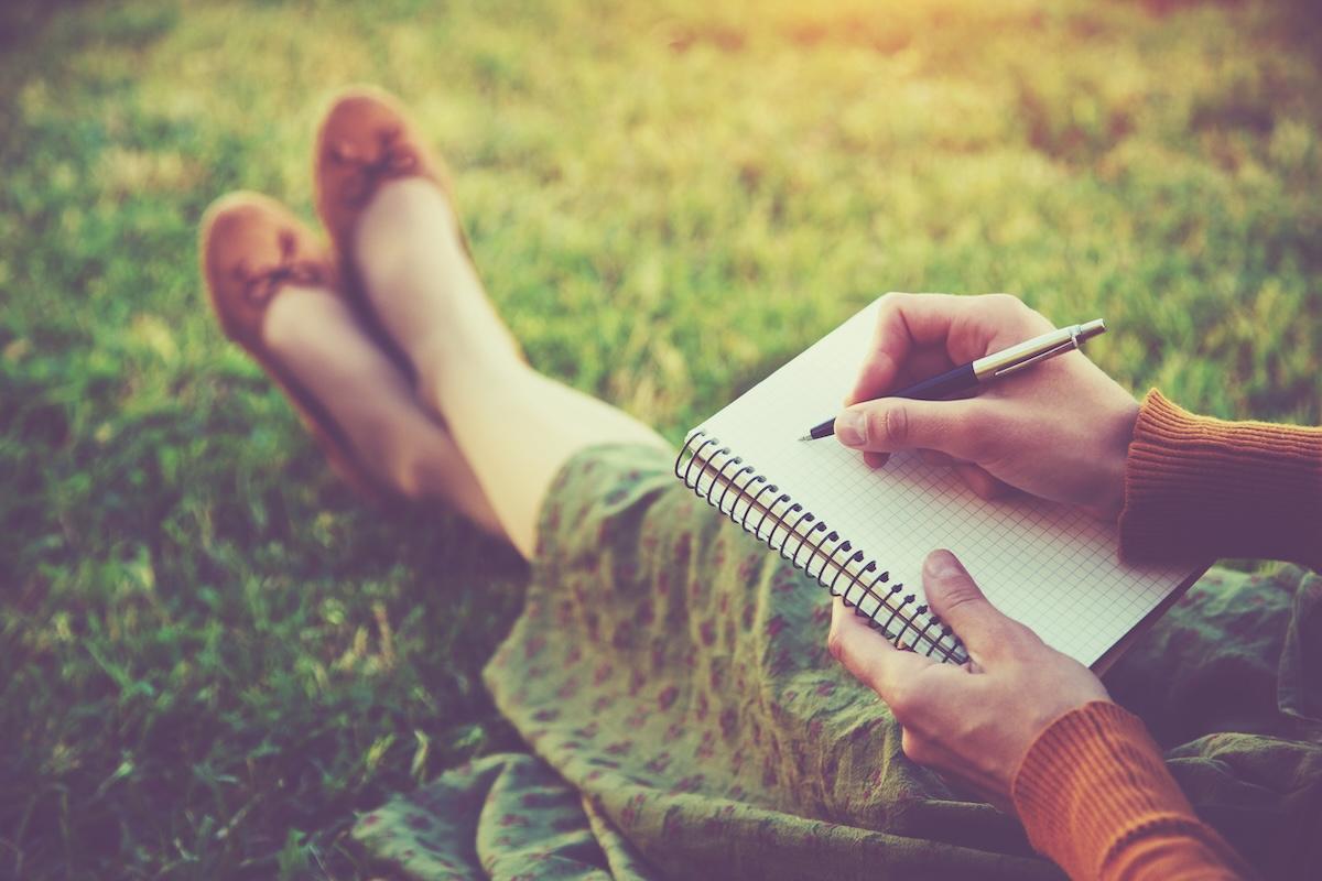 person sitting on grass with journal about to write
