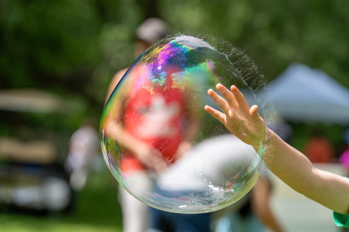 child hand touching a large bubble just before it pops