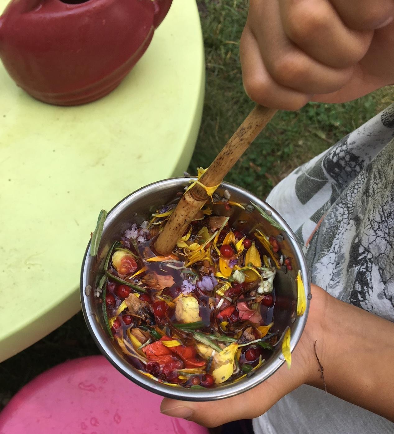 youth hand holding a bowl filled with a play potion of flower petals and water