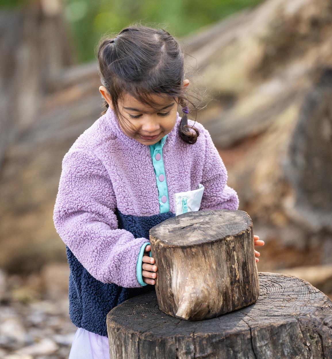 child stacks a log onto another larger log