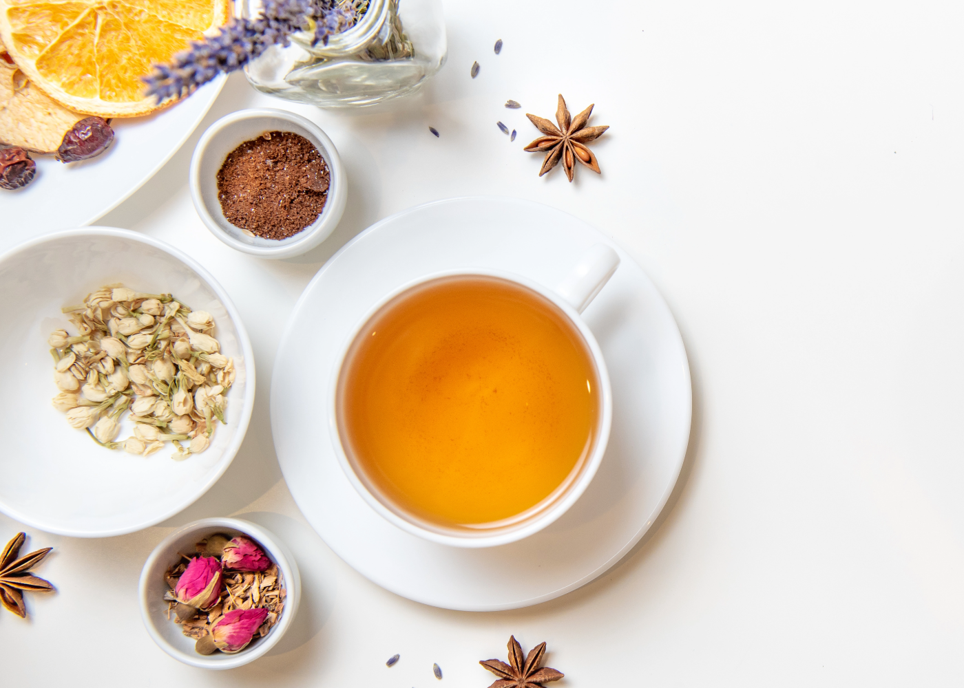 a cup of tea with small bowls of herbs and slices of citrus next to it