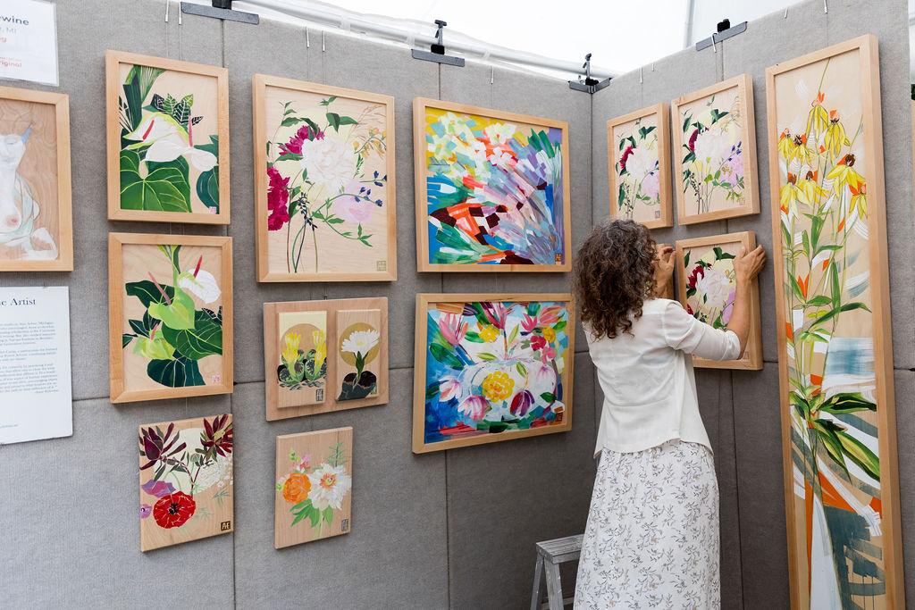 Anne Erlewine hanging a floral painting in a wall with other floral pieces hanging