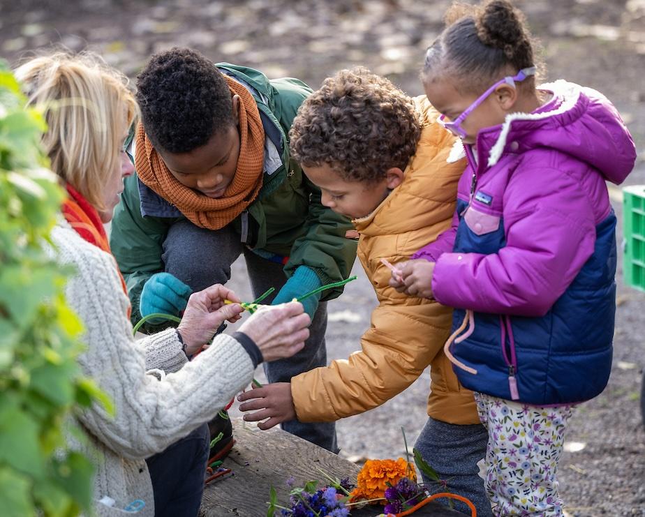MBGNA's Lee Smith Bravender offers crafting materials to three children dressed in winter coats outdoors.
