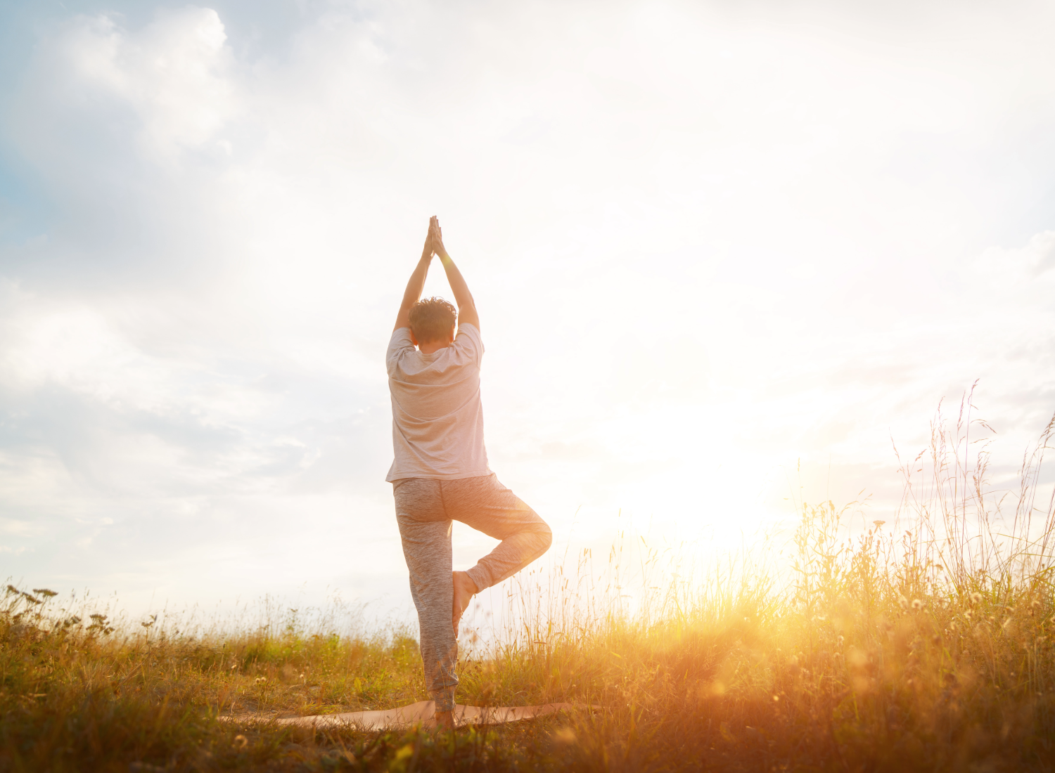 Person outside in field with setting sun doing a standing yoga pose