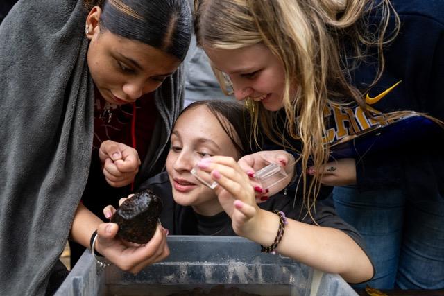 three teens look at a rock with smiles