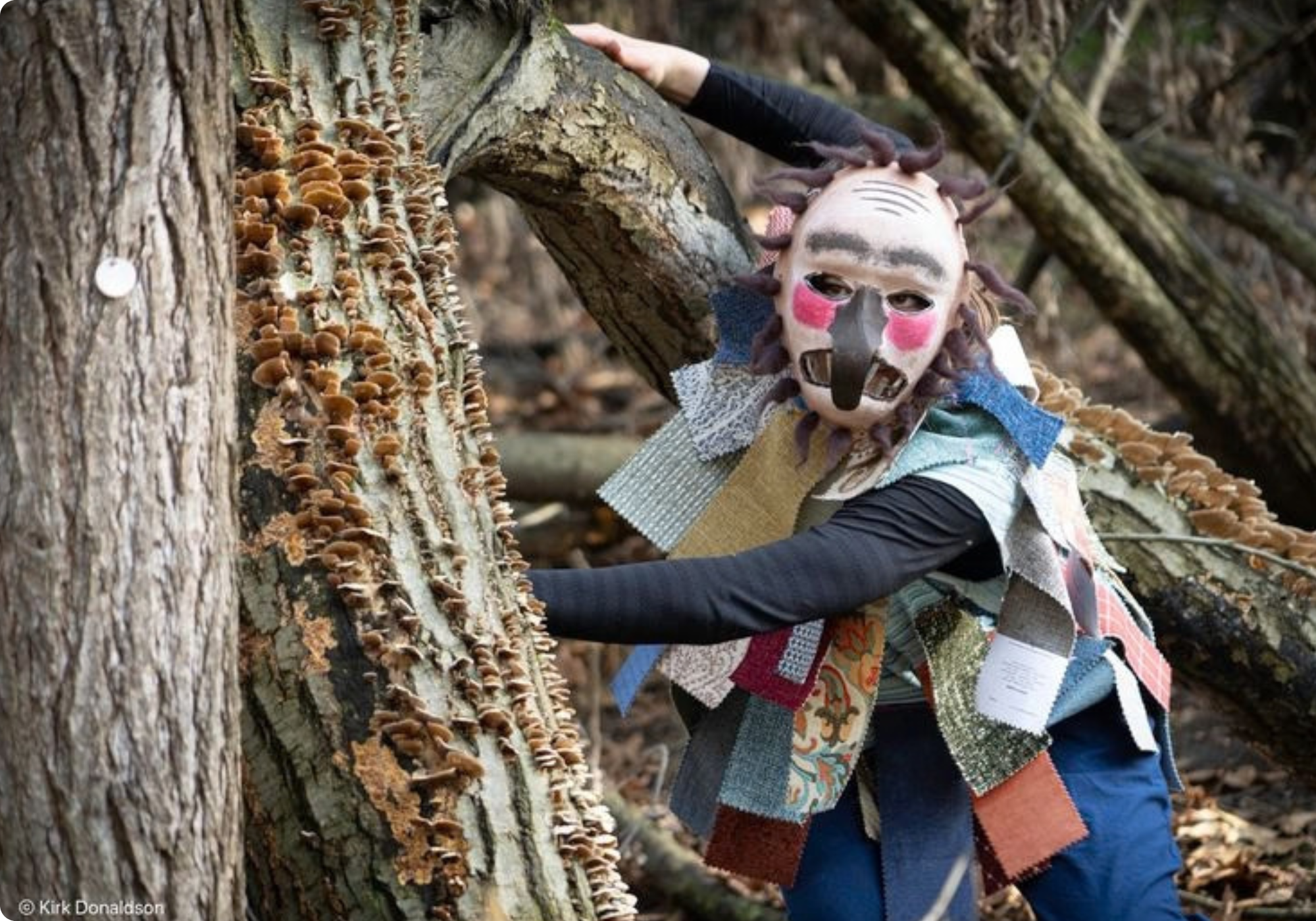 person in a colorful mask by a tree