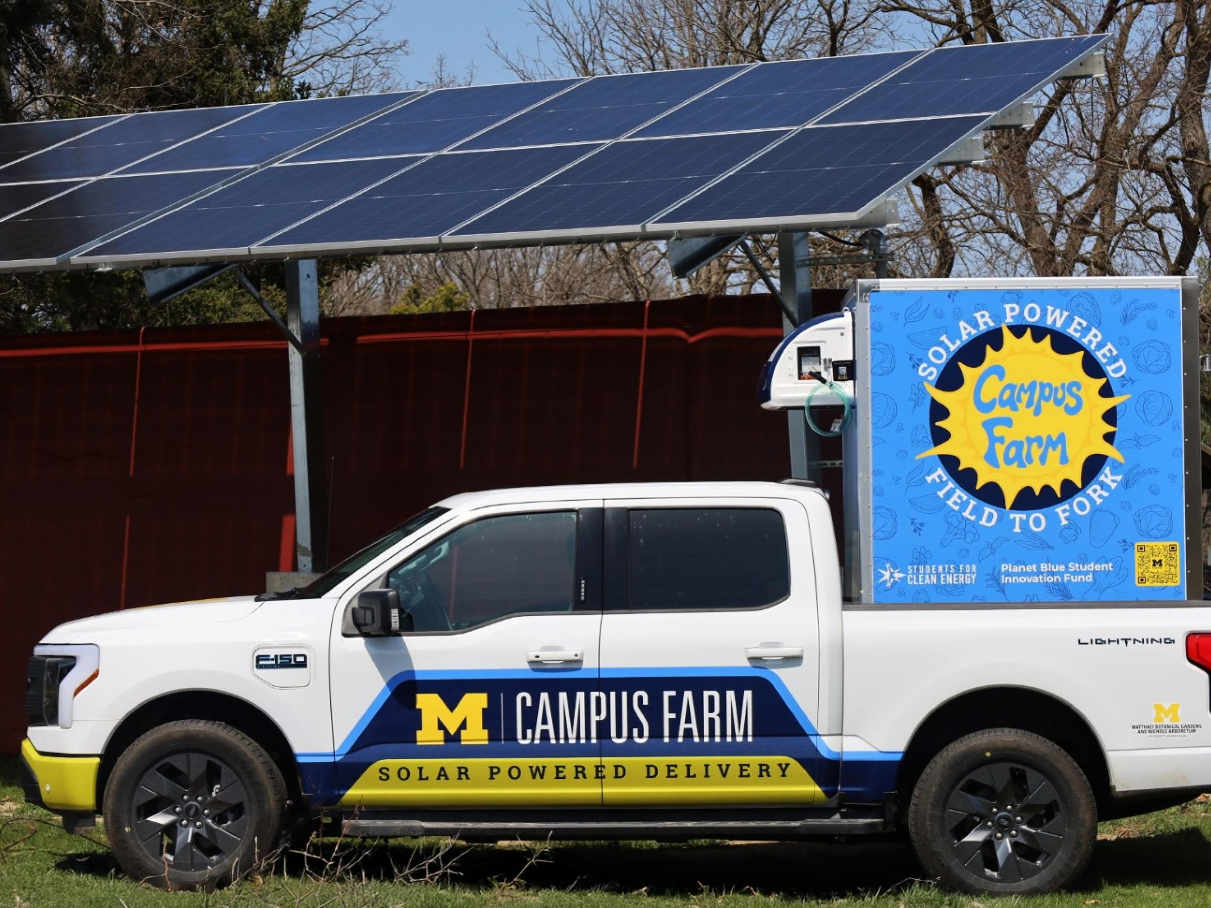 The EV truck parked in front of the solar panels that charge it at the Campus Farm