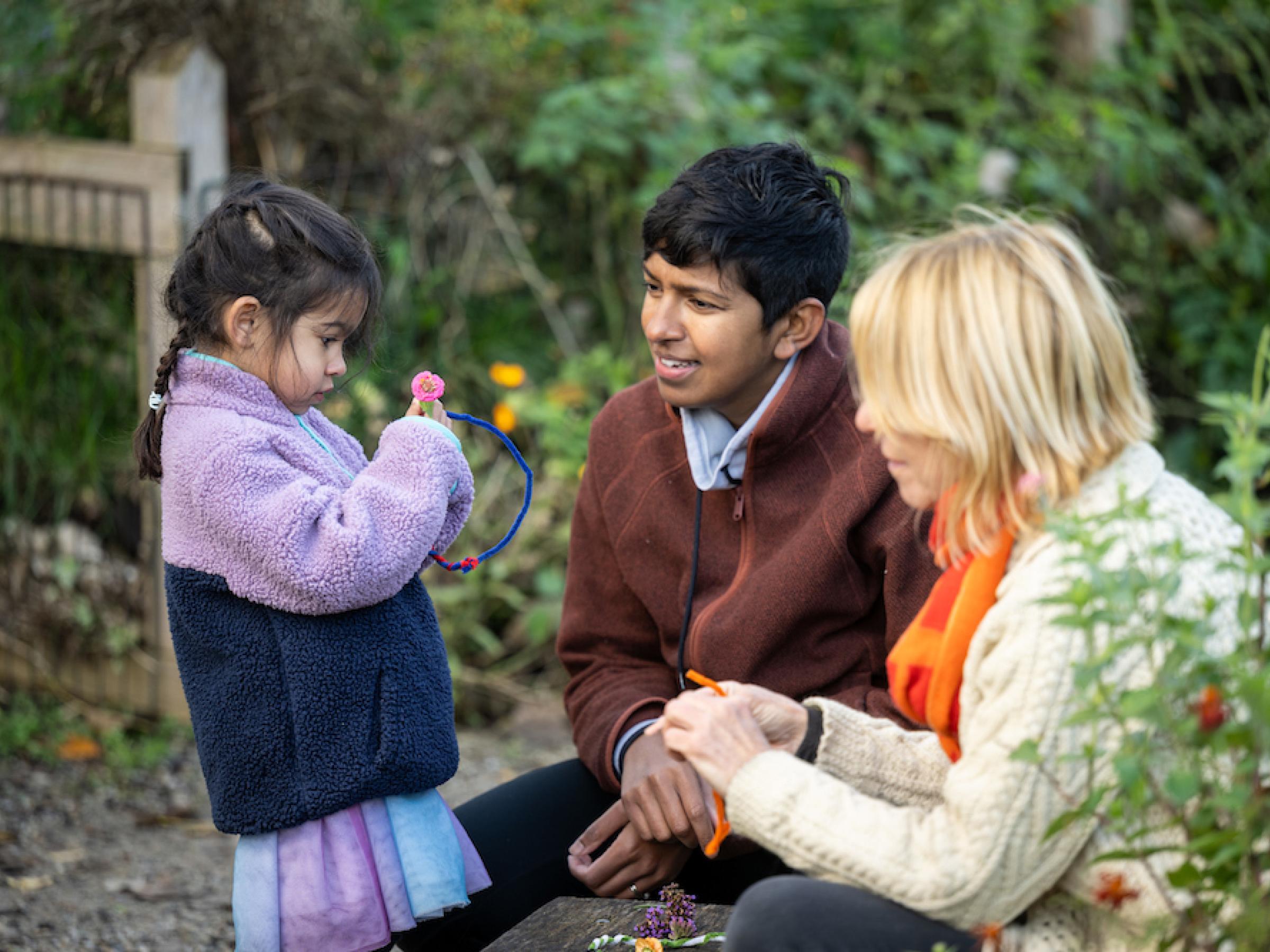 A child showing a small flower to two adults