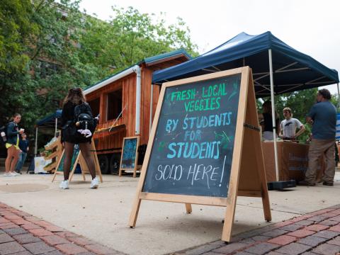 An a-frame chalk board with text "fresh local veggies for students by students" sits in front of new farm stand