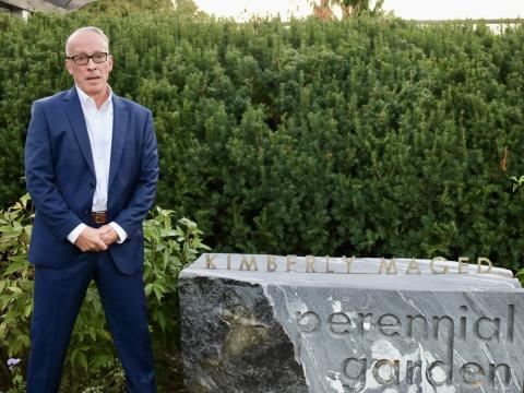 Ted Maged standing in front of stone that says "Kimberly Maged Perennial Garden"