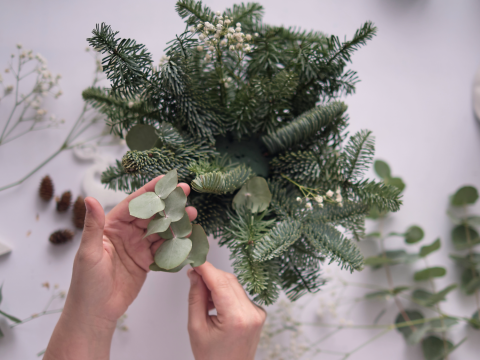 pair of hands putting together an arrangement of holiday greens 