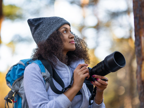 person in winter hat and jacket lookin up while holding a long camera