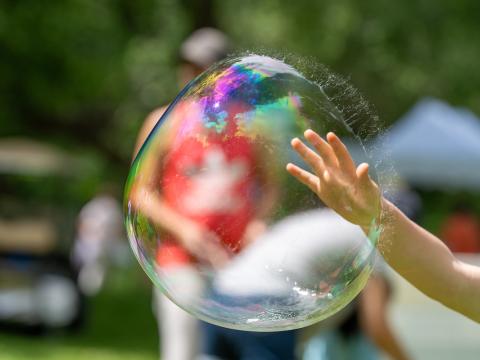 child hand touching a large bubble just before it pops