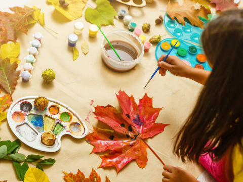 back of child making nature art with leaves and paint