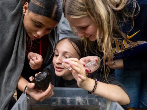 three teens look at a rock with smiles