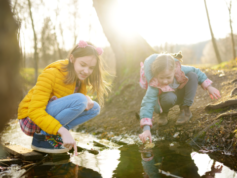 two children playing at waters edge in wooded space