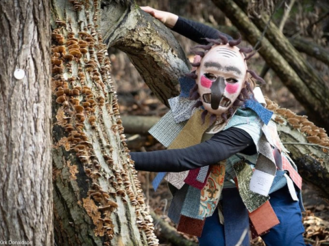 person in a colorful mask by a tree