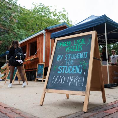 An a-frame chalk board with text "fresh local veggies for students by students" sits in front of new farm stand