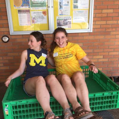 Two MBGNA interns laughing as they sit in a green yard cart