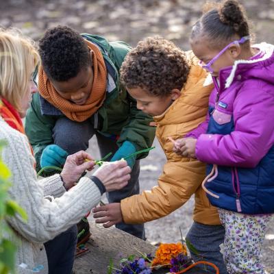 MBGNA's Lee Smith Bravender offers crafting materials to three children dressed in winter coats outdoors.