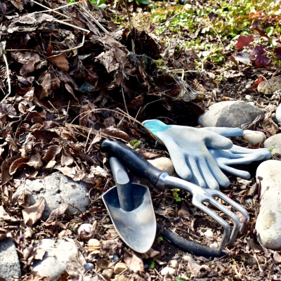 Garden gloves and trowel on ground next to a pile of dead leaves